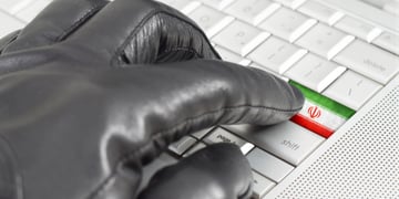 Hacking Iran concept with hand wearing black leather glove pressing enter key with flag overlaid
